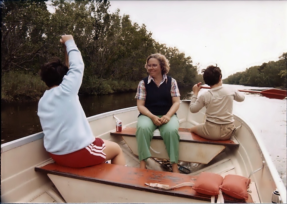 Faust’s mom smiling in a boat with Faust and his brother, one raising an arm and the other paddling